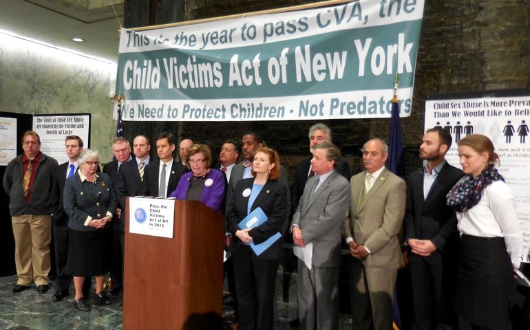 People standing at a podium with a banner that reads, "Child Victims Act of New York."