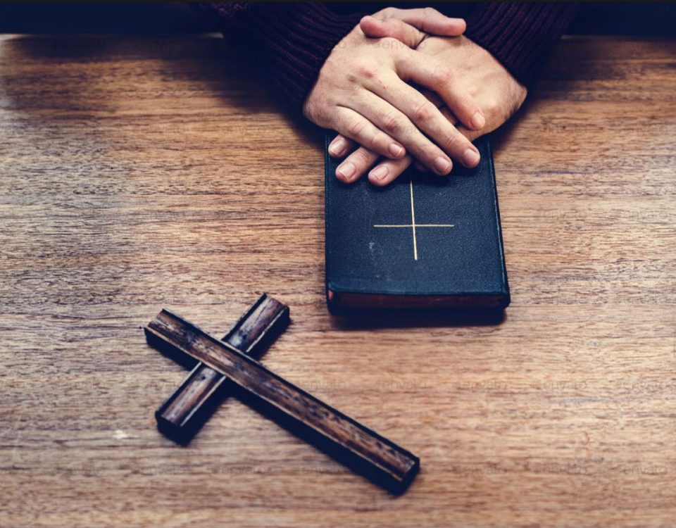 A Person with a bible and a wooden cross on a table.