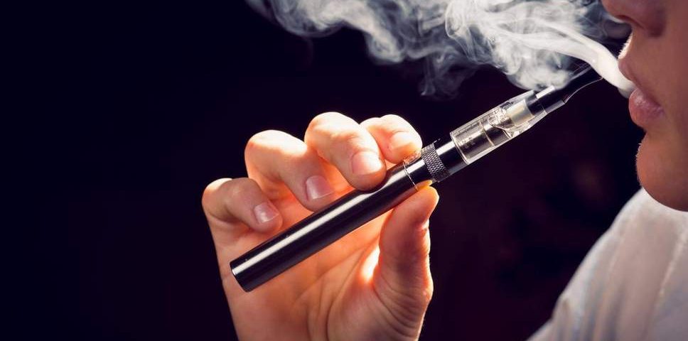 A person vaping a e-cigarette with a cloud of vapor surrounding them.