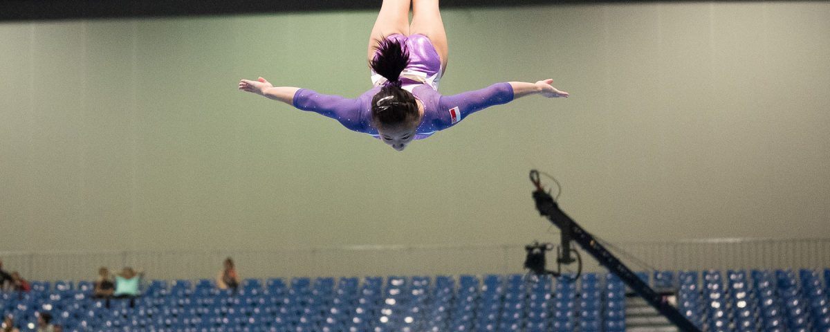 A young woman gymnast is flying through the air doing a gymnastic stunt.