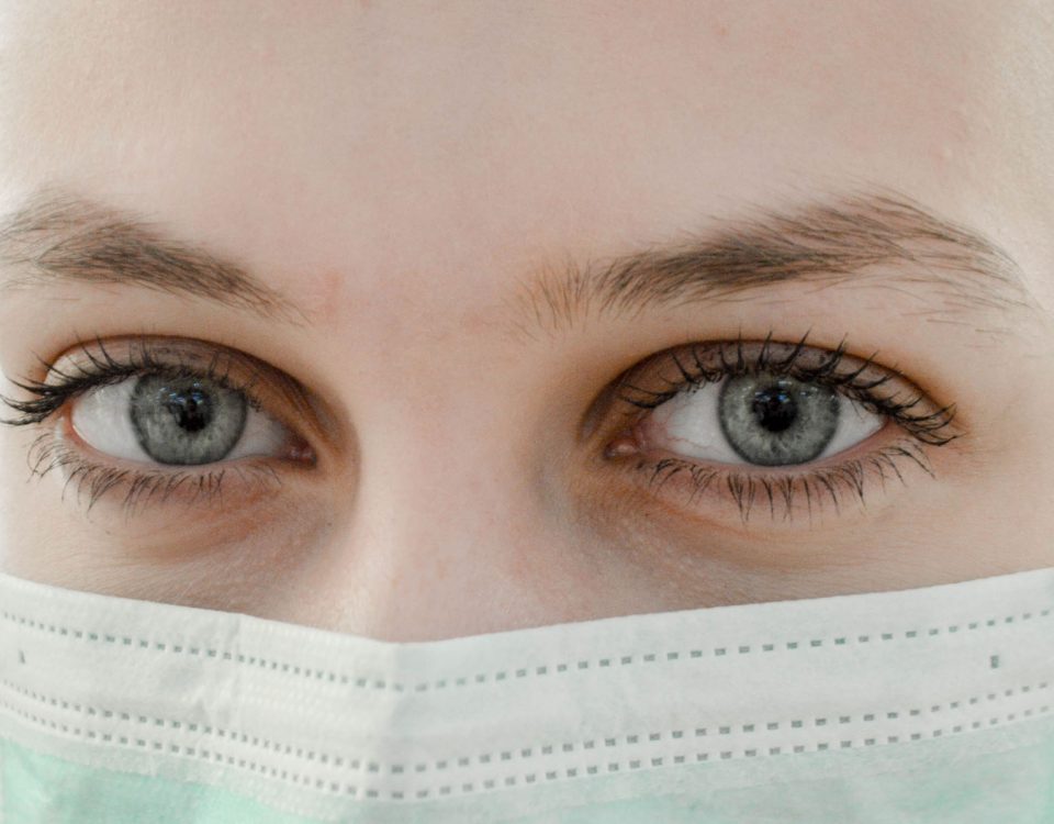 A close up shot of a persons eyes, and a medical mask over their nose and mouth.