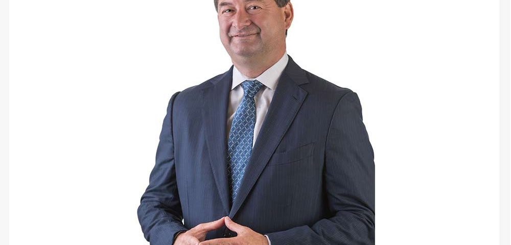 A lawyer named Brian Aylstock wearing a suit with a blank background looking into the camera.